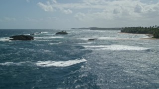 AX101_204E - 4.8K aerial stock footage flying low above sparkling waters toward rock formations along the coast, Vega Baja, Puerto Rico