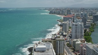 AX102_002E - 4.8K aerial stock footage of flying over and by hotels and high rises on the coast and crystal blue water, San Juan, Puerto Rico