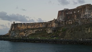 AX104_081E - 4.8K aerial stock footage flying along the walls of Fort San Felipe del Morro, Old San Juan, twilight