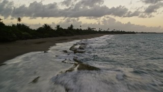 AX104_098E - 4.8K aerial stock footage fly over the show and blue Caribbean waters along a coastal highway with palm trees, Dorado, Puerto Rico, twilight