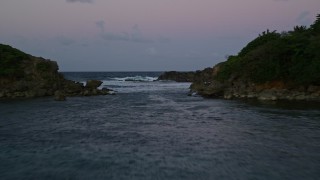 AX104_122E - 4.8K aerial stock footage flying over ocean and through a gap in the coast, Dorado, Puerto Rico, twilight