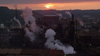 AX108_033E - 4K aerial stock footage of U.S. Steel Mon Valley Works seen while ascending past a bridge, Braddock, Pennsylvania, sunset