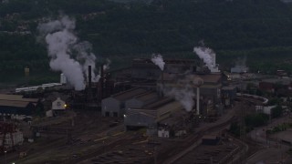 AX108_038E - 4K aerial stock footage of smoke rising from the U.S. Steel Mon Valley Works, Braddock, Pennsylvania, twilight