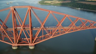 AX111_080E - 5.5K aerial stock footage of approaching a commuter train on Forth Bridge in Scotland