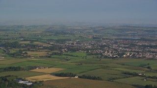 AX113_006E - 5.5K aerial stock footage of farming fields near rural residential neighborhoods in Glasgow, Scotland at sunrise