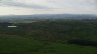 AX113_051E - 5.5K aerial stock footage of flying by hilly moorland, reveal farms, Maybole, Scotland