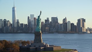 AX118_131E - 5.5K aerial stock footage approach the Statue of Liberty at sunrise in New York, and flyby for a view of Lower Manhattan skyline