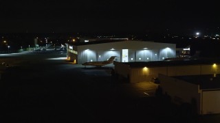 AX123_191E - 5.5K aerial stock footage of civilian jets parked outside a hangar at Night at Republic Airport in Farmingdale, New York