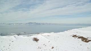 5.5K aerial stock footage of the Great Salt Lake seen from snowy mountain summit on Antelope Island, Utah Aerial Stock Footage | AX125_038E