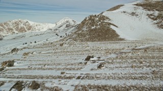 5.5K aerial stock footage fly over rocky ground and snow up the slopes of mountains in winter, Antelope Island, Utah Aerial Stock Footage | AX125_086E