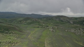 5.5K aerial stock footage of flying by green hills, trees, heavy clouds above, Wasatch Range, Utah Aerial Stock Footage | AX130_127E