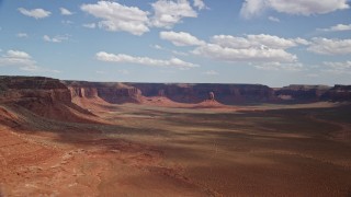 AX132_097E - 5.5K aerial stock footage of approaching butte in wide valley by mesas, Navajo Nation Reservation, Arizona, Utah