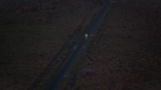 AX134_068E - 5.5K aerial stock footage of tracking SUV on highway in desert valley, Monument Valley, Utah, Arizona, twilight