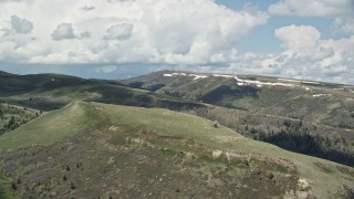 AX140_032E - 5.5K aerial stock footage flyby mountains with patches of snow under partly cloudy skies, Utah County, Utah