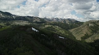 5.5K aerial stock footage of passing by green mountains, snowy peaks in the distance, Wasatch Range, Utah Aerial Stock Footage | AX140_225E