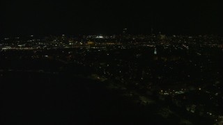 AX141_226E - 5.5K aerial stock footage flying by Dorchester Heights Monument, skyline, South Boston, Downtown Boston, Massachusetts, night