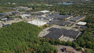 AX143_006E - 5.5K aerial stock footage flying over forest, approach warehouse buildings, autumn, Braintree, Massachusetts