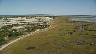 AX143_138E - 5.5K aerial stock footage flying over coastal road, marshland, sand dunes, Barnstable, Massachusetts