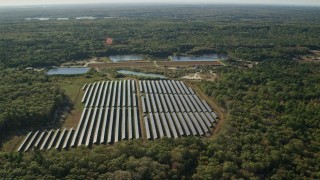 AX144_212E - 6k aerial stock footage approaching solar array, dense trees, Dartmouth, Massachusetts