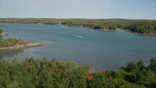 AX148_014E - 6K aerial stock footage flying over colorful forest, approach boat on Damariscotta River, autumn, Newcastle, Maine