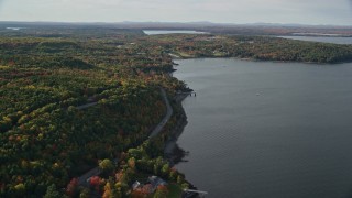 5.5K aerial stock footage flying over water toward rode winding through forest with partial fall foliage, Bar Harbor, Maine Aerial Stock Footage | AX148_224E