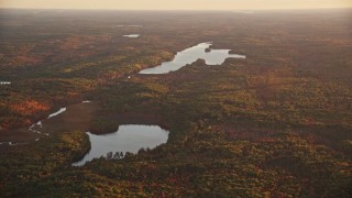 AX149_200E - 5.5K aerial stock footage flying by James Pond and Long Pond, forest in autumn, Palermo, Maine, sunset