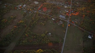 AX149_213 - 5.5K aerial stock footage of a bird's eye view over rural homes and intersection, autumn, Augusta, Maine, sunset