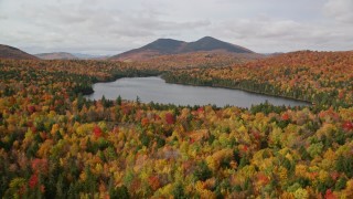 AX150_153E - 5.5K aerial stock footage flying over autumn forest, descend and fly over Mountain Pond, White Mountains, New Hampshire