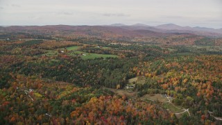 AX150_312E - 5.5K aerial stock footage flying over colorful forest, approaching small farms, autumn, Ryegate, Vermont