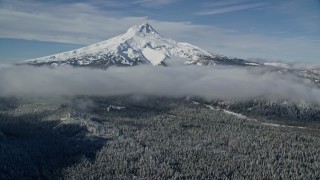 AX154_118E - 5.5K aerial stock footage of snowy mountain peak with low clouds over forest, Mount Hood, Cascade Range, Oregon