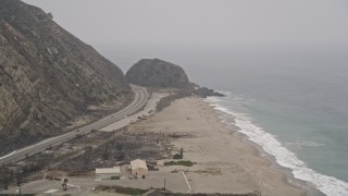 AX42_057E - 5K aerial stock footage of following Highway 1 over an empty beach toward a rock formation, Point Mugu, California