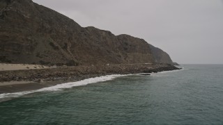 AX42_067E - 5K aerial stock footage of waves crashing into the coast by Highway 1, Malibu, California