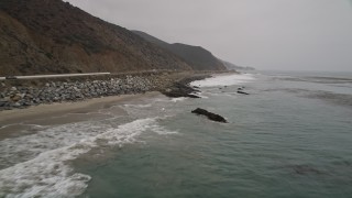 AX42_073 - 5K aerial stock footage of flying low over waves rolling toward the coast and Highway 1, Malibu, California