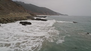 AX42_074E - 5K aerial stock footage fly low over ocean kelp to approach waves crashing into the coast, Malibu, California