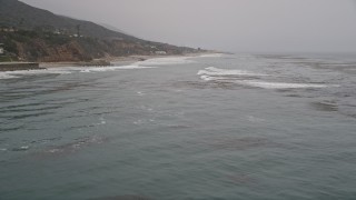 AX42_080 - 5K aerial stock footage fly low over the ocean to approach waves rolling toward a beach, Malibu, California