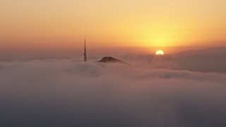 4K aerial stock footage of the sunset behind Hollywood Hills, radio tower covered in Marine Layer, California Aerial Stock Footage | AX44_031