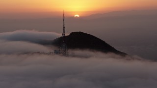 4K aerial stock footage of sun setting behind Hollywood Hills and radio tower in marine layer, California Aerial Stock Footage | AX44_032E