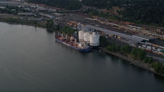 AX54_027 - 5K aerial stock footage approach oil tanker beside a silo and train yard, Willamette River, North Portland, Oregon, sunset