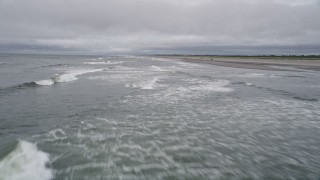 AX56_124E - 5K aerial stock footage of a low altitude flight over crashing waves near an empty beach in Ilwaco, Washington