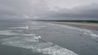 AX56_136E - 5K aerial stock footage of ocean waves rolling toward a beach with a few people on the shore in Long Beach, Washington