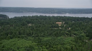 AX58_052E - 5K aerial stock footage fly over rural homes in an evergreen forest, and approach Colvos Passage, Olalla, Washington