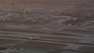 AX69_012 - 4.8K aerial stock footage track airliner on runway and tilt to reveal control tower and terminals at LAX at twilight, Los Angeles, California