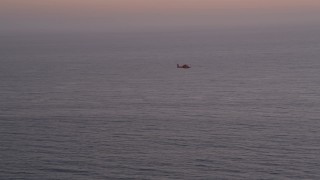 AX69_043 - 4.8K aerial stock footage of tracking a Coast Guard helicopter over the Pacific Ocean at twilight