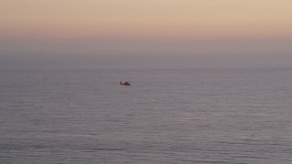 AX69_044 - 4.8K aerial stock footage track a Coast Guard helicopter flying over the Pacific Ocean at twilight