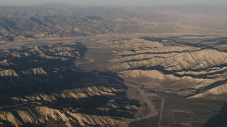 AX70_026 - 4K aerial stock footage Dry riverbed between rugged mountain ridges at sunrise, Cuyama, California, farms in background