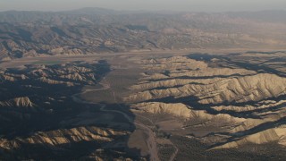 AX70_027 - 4K aerial stock footage Farms beyond a dry riverbed between rugged mountain ridges at sunrise, Cuyama, California