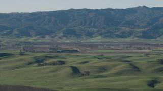 4K aerial stock footage Green hills and farms with mountains in the background in Hollister, California Aerial Stock Footage | AX70_111