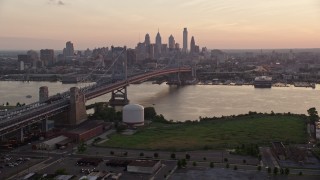 4.8K aerial stock footage fly next to the Benjamin Franklin Bridge over Delaware River toward Downtown Philadelphia skyline, Pennsylvania, Sunset Aerial Stock Footage | AX80_136E