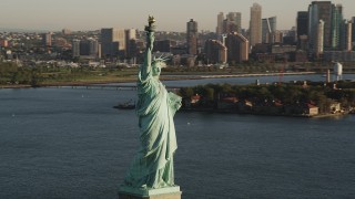 AX90_142 - 4K aerial stock footage of Statue of Liberty, Liberty Island, reveal Midtown Manhattan, New York, sunrise