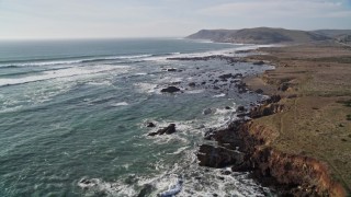 AXSF03_012 - 5K aerial stock footage fly over grassland, coastal cliffs and empty beach, and tilt up to follow the coast, Estero Bay, California